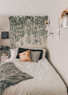 a white bed topped with pillows next to a green plant wall hanging on the wall