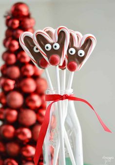 chocolate covered candy sticks with reindeer noses and red ribbon tied around them in front of a christmas tree