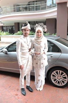 two people standing in front of a car wearing white outfits and headdresss