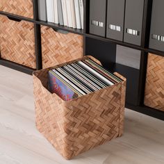 a basket with records in it sitting on the floor next to a bookcase filled with books