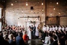 a group of people standing in front of a crowd at a wedding ceremony with lights hanging from the ceiling