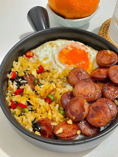 a bowl filled with rice and sausage next to an orange on the table, along with other food items