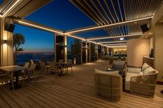 an outdoor deck with wicker furniture and lights at night time, overlooking the ocean