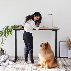 a woman standing at a table with a dog sitting next to her on the floor