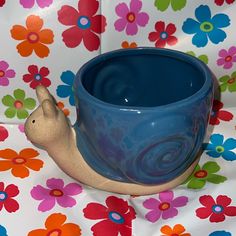 a blue cup sitting on top of a flowery tablecloth with a snail figurine next to it