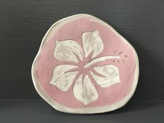 a pink and white plate with a flower painted on the side, against a black background