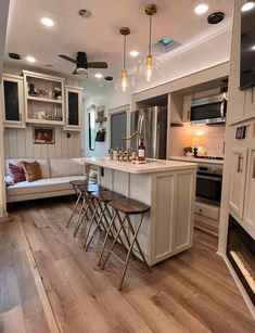 an open concept kitchen and living room with wood flooring, white cabinets, stainless steel appliances and bar stools