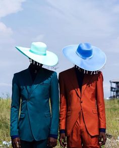 two men in suits and hats standing next to each other on a field with tall grass