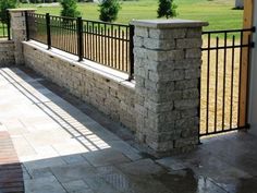 a stone wall and iron fence in front of a house with a green field behind it