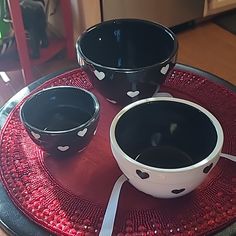 two black and white bowls sitting on top of a red plate with hearts painted on it