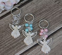 three keychains with angel charms on them sitting on a wooden table next to flowers