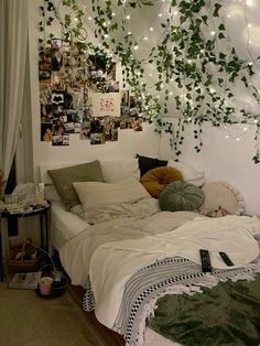 an unmade bed with lots of plants hanging from the ceiling and lights on the wall