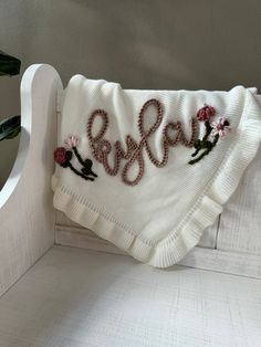 a white blanket with embroidered letters and flowers on it