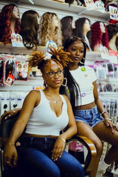 two women sitting on chairs in front of shelves with wigs and other hair products