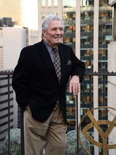 an older man wearing a suit and tie standing on a balcony