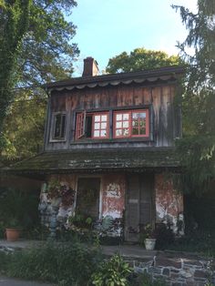 an old wooden house with red windows and shutters on the outside, surrounded by greenery