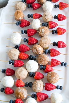 strawberries and blueberries are arranged on skewers with marshmallows