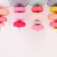 colorful paper fans hanging from the ceiling in front of a white wall with pink, blue, yellow and green decorations