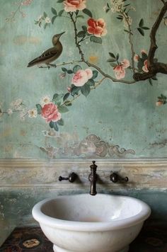 a white sink sitting in front of a wall with flowers and birds painted on it