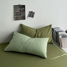 a bed with green sheets and pillows next to a book shelf filled with books on top of it