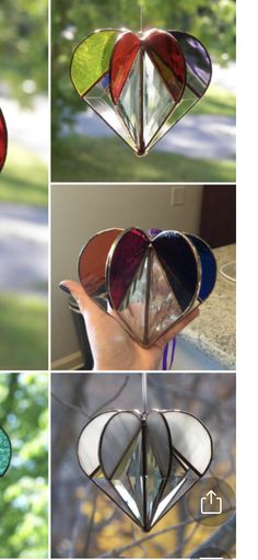 four different colored glass hearts hanging from a wire in the shape of a heart, with trees and grass behind them