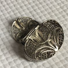 an ornately designed silver metal object on a white surface with checkered fabric in the background