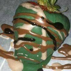 a green apple with chocolate drizzled on it's side and a strawberry in the middle