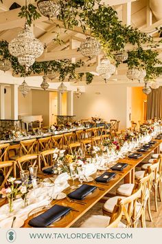 a long table set up with place settings and hanging chandeliers for an event