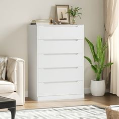 a white chest of drawers sitting in a living room next to a chair and potted plant