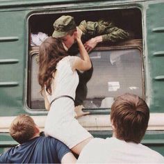 two people are looking out the window of a train while another person is holding something in their hand