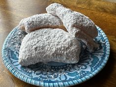 powdered sugar covered pastries sit on a blue and white plate atop a wooden table