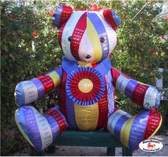 a large teddy bear sitting on top of a green bench in front of some bushes