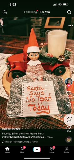 an elf is sitting on top of a table with a sign in front of him