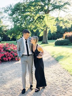 a man and woman standing next to each other in front of some bushes with pink flowers