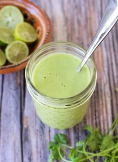 a glass jar filled with green liquid next to a bowl of limes and cilantro