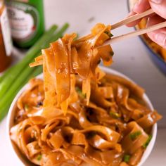 a person holding chopsticks over a bowl of noodles with sauce and green onions