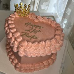 a heart shaped cake decorated with pink icing and a gold tiara on top