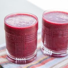 two glasses filled with red smoothie sitting on top of a table next to each other