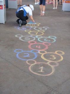 a person kneeling down on the ground drawing numbers with chalk in front of them and people standing around