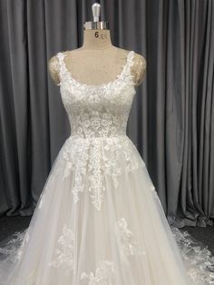 a white wedding dress on display at a bridal shop in front of grey curtains