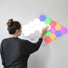 a woman is touching the colorful hexagonal wall light