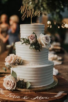 a white wedding cake with flowers on top and the word mr and mrs written on it