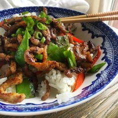 a blue and white plate topped with meat and veggies next to chopsticks