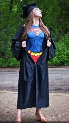 a woman in a graduation gown and cap is looking up at the sky while wearing a superman cape