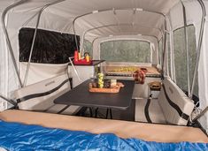 the inside of a camper with a table and chairs in it, next to a sleeping bag