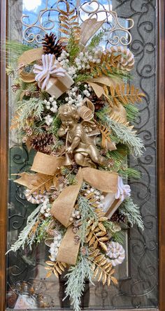 a christmas wreath with pine cones, evergreens and gold ribbon hanging on a door