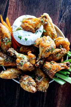 chicken wings with ranch dressing and carrots in a bowl on top of a wooden table