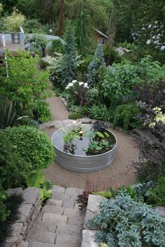 a garden filled with lots of plants next to a walkway and water feature in the middle