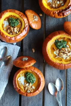 three pumpkins filled with different types of food on top of a wooden table next to silver spoons