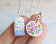 a hand holding two necklaces with different designs on them, one has a milk carton and the other is a doughnut